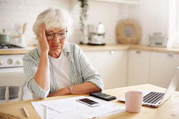 Sad frustrated senior woman pensioner having depressed look holding hand to her face.